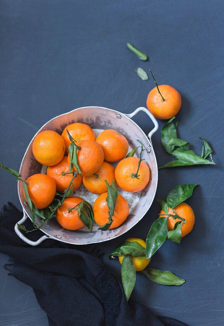 Fresh tangerines in a metal bowl against a blue background (top view)