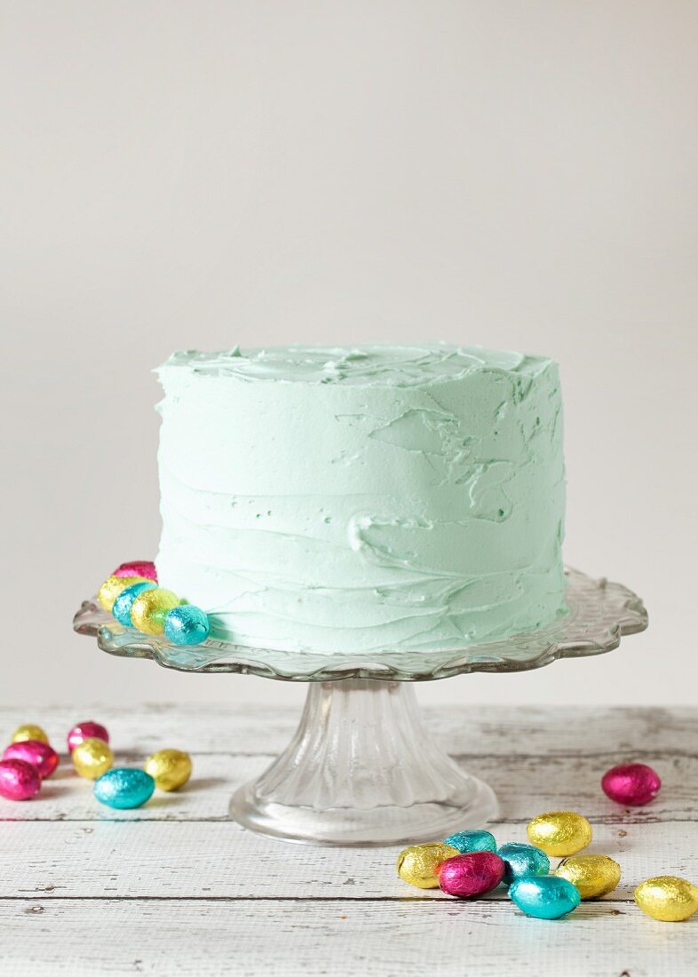 A pastel green buttercream layered cake with foil-wrapped mini chocolate eggs