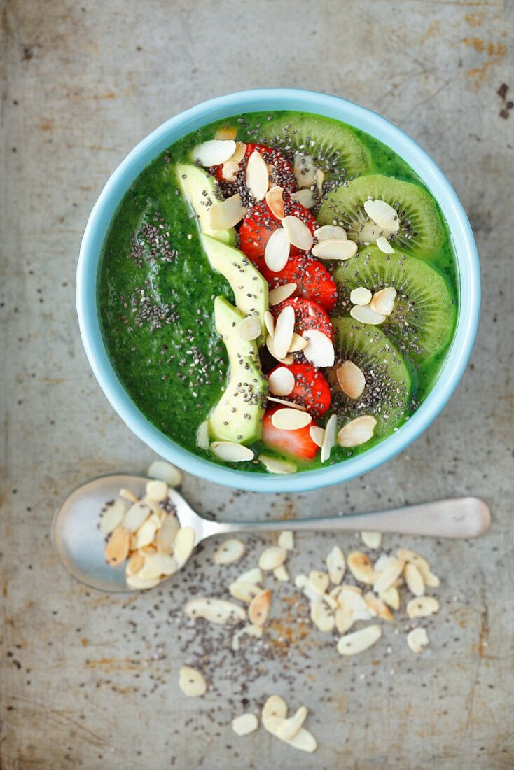A smoothie bowl with spinach, kiwi, strawberries, apple and flaked almonds