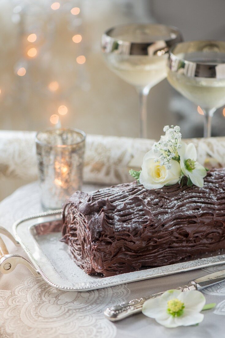 A festive chocolate log decorated with white flowers on a silver serving platter
