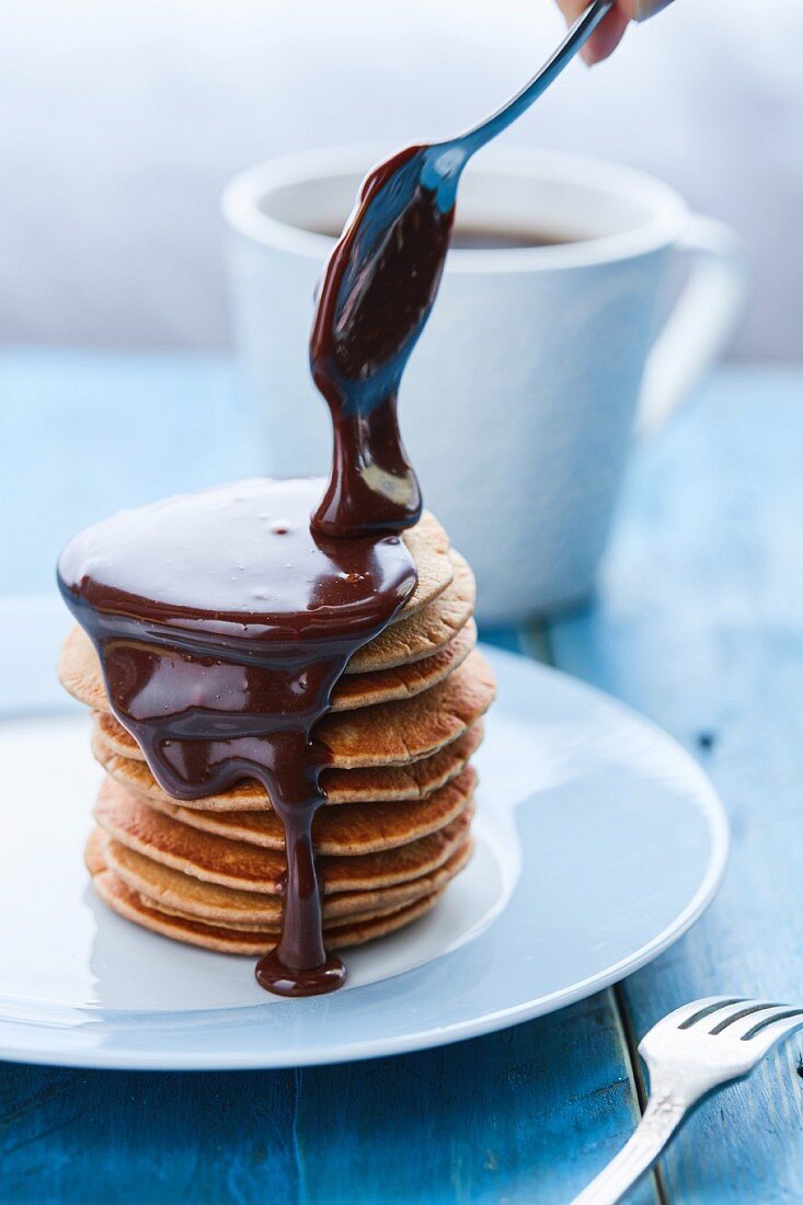 Chocolate sauce dripping off a spoon over a stack of pancakes