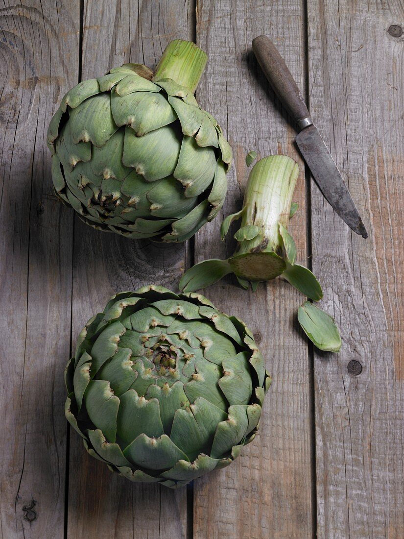 Two fresh artichokes with a knife on a wooden background