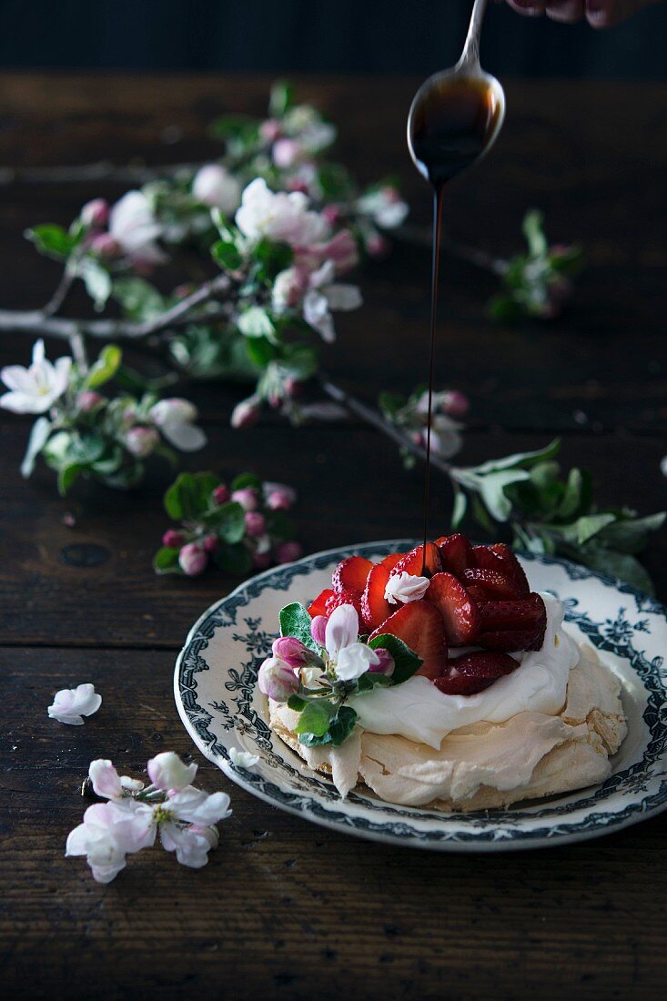 Crema di Balsamico fliesst auf Erdbeer-Pavlova dekoriert mit Obstblüten