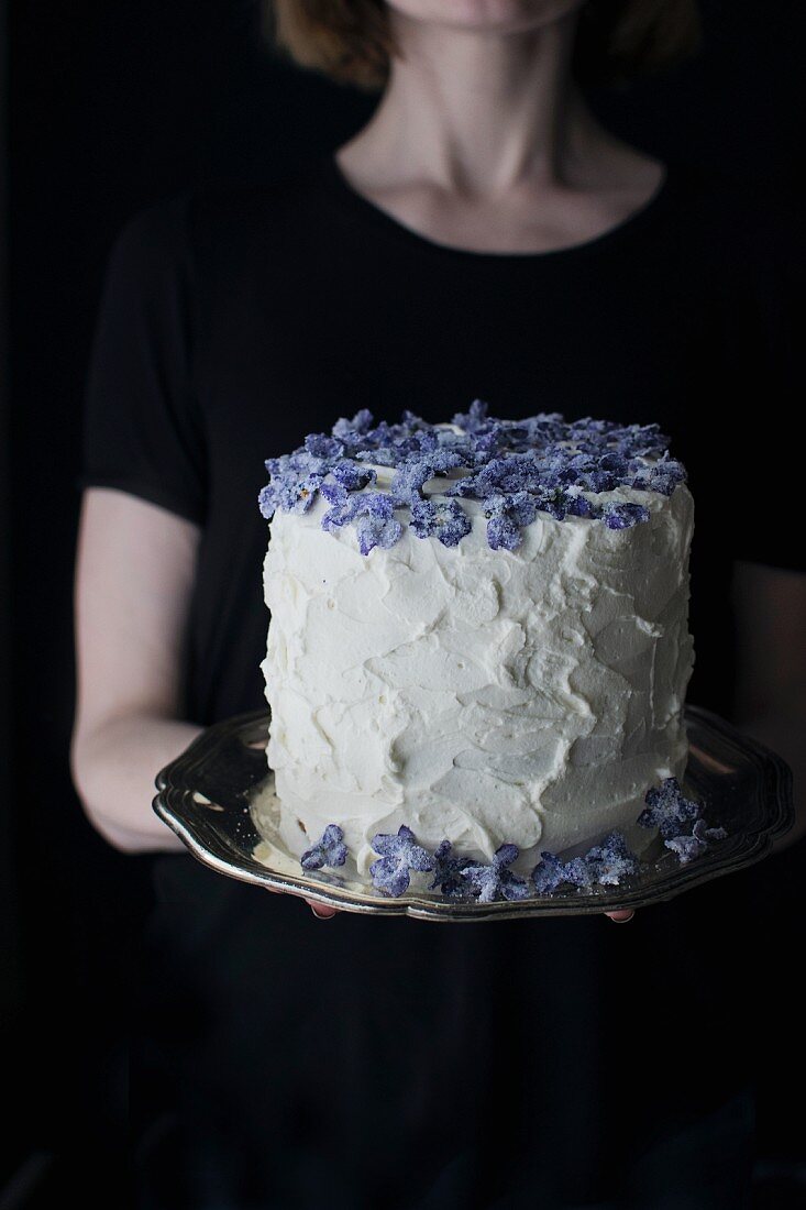 A woman serving a mascarpone cream cake with candied violets