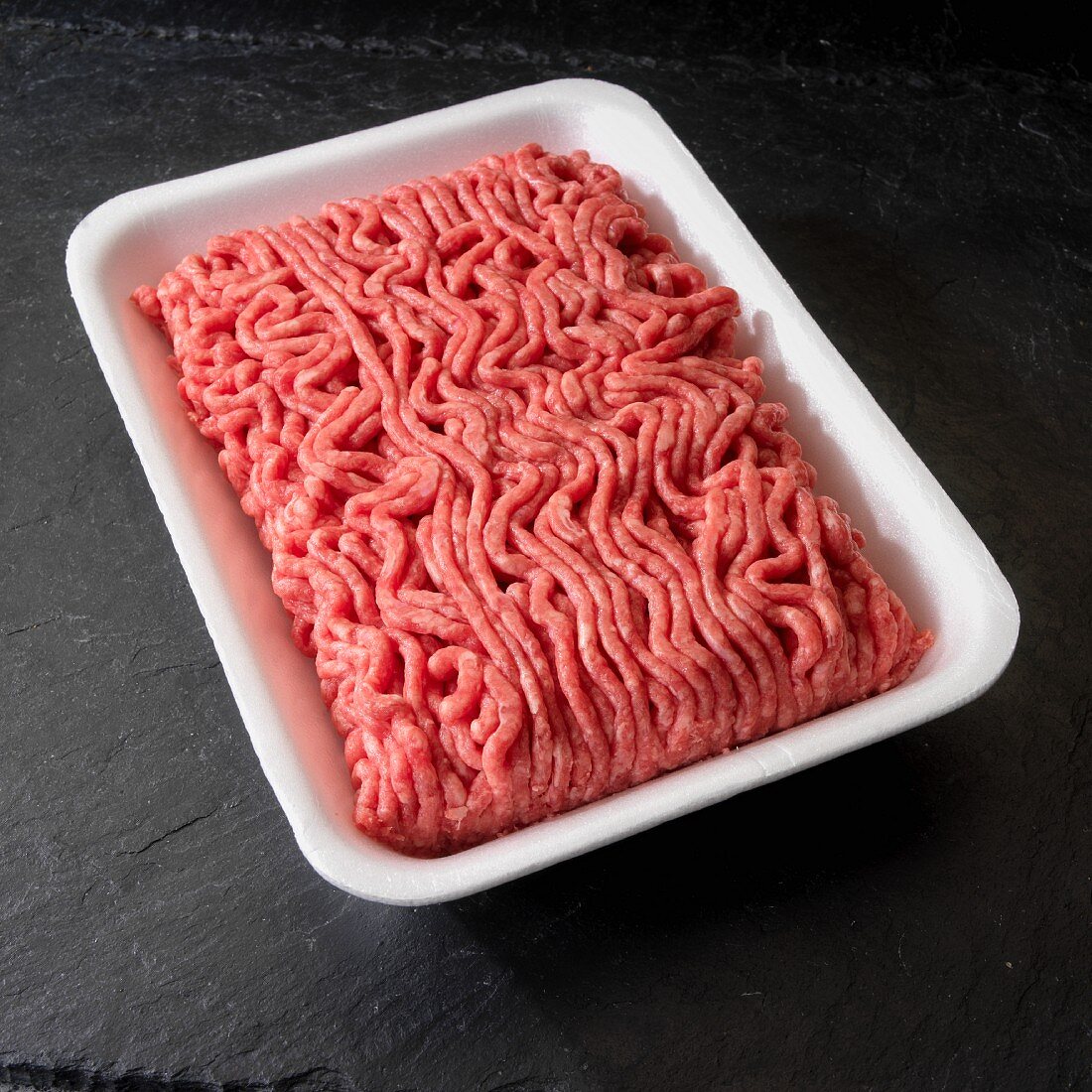 Ground beef in white tray on black background