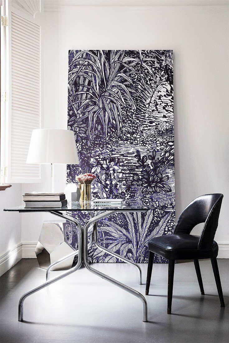 Black leather chair, glass table and large picture in elegant, minimalist study