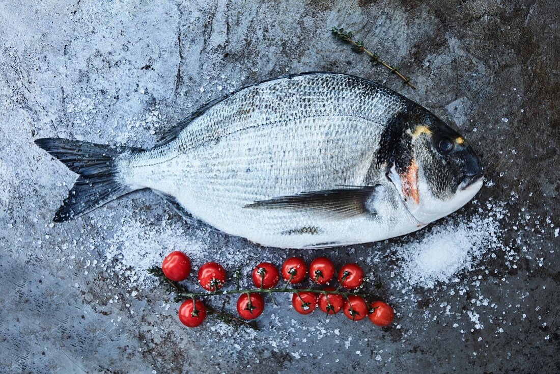 Fresh sea bream next to cherry tomatoes and salt