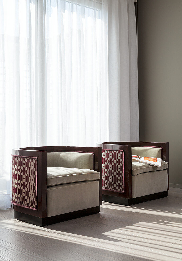 Two designer armchairs in front of window with floor-length curtains