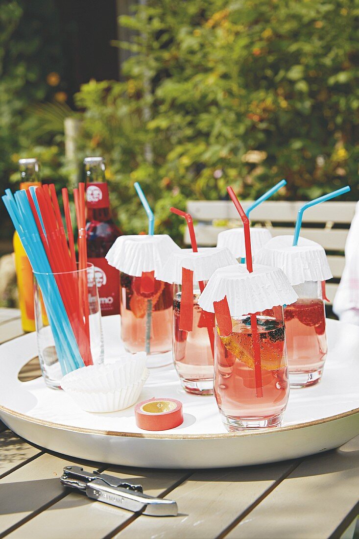 Getränke in Gläsern mit Papierdeckel und Strohhalm auf Gartentisch