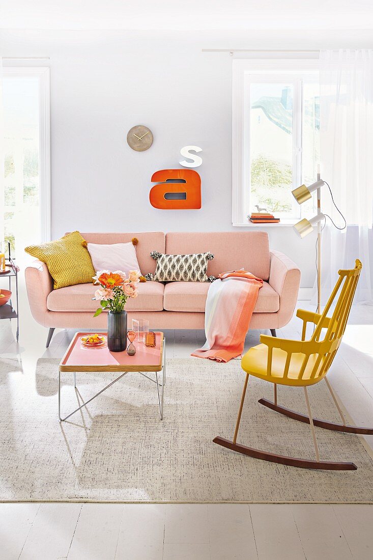 A living room with a pale pink sofa, a tray table and a yellow rocking chair