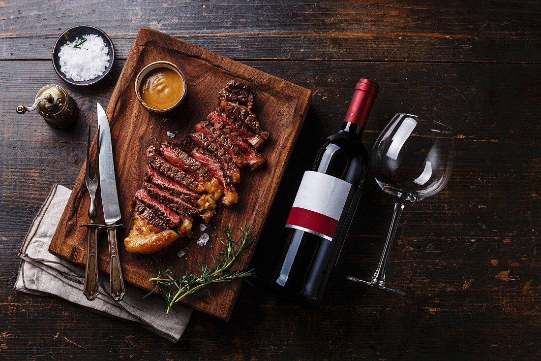 Grilled sliced Steak Striploin with Pepper sauce and bottle of Red wine on wooden background
