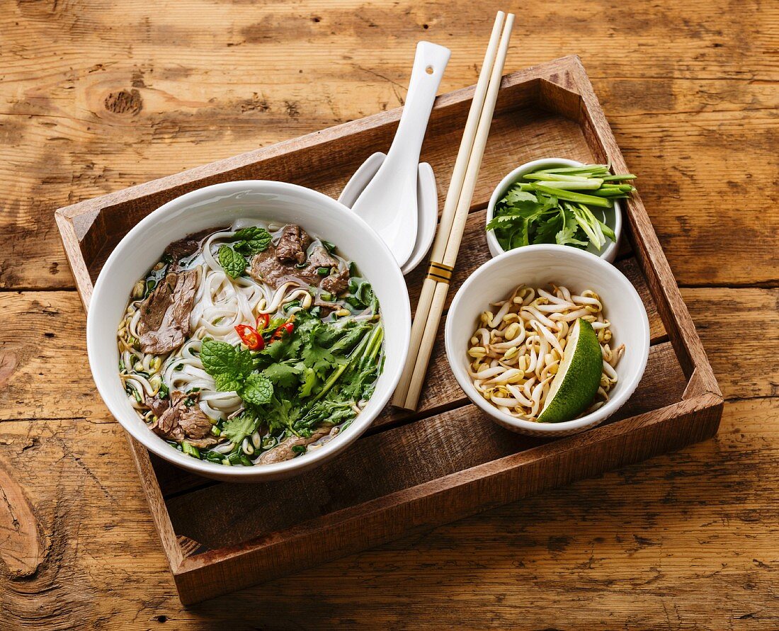 Pho Bo (Suppe mit Rindfleisch, Reisnudeln und Sprossen, Vietnam) auf Holztablett