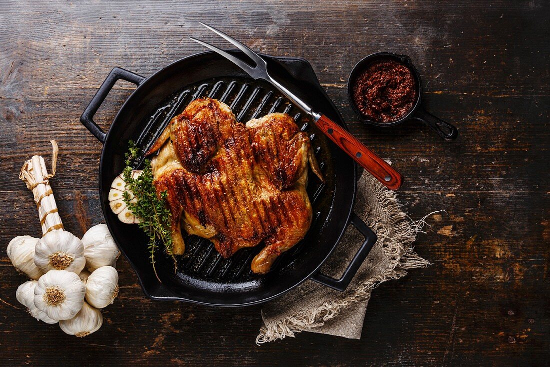 Grilled fried roast Chicken Tabaka in frying pan on wooden background