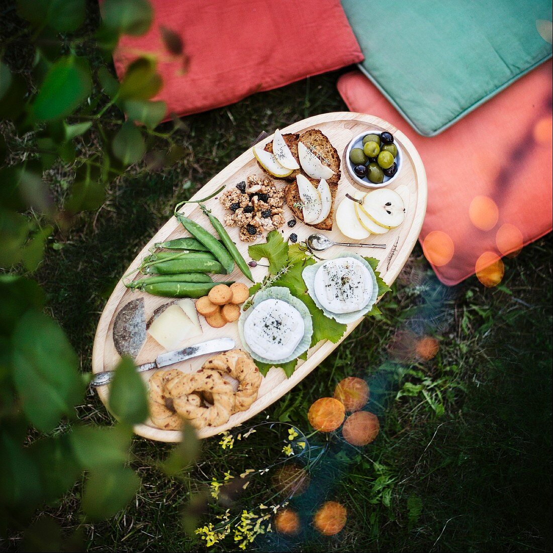 Picknickplatte mit Gebäck, Gemüse, Obst, Nüssen und Käse im Gras (Aufsicht)