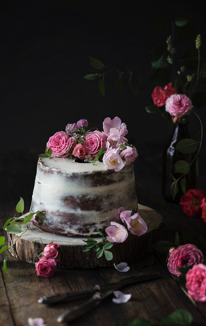 Naked Cake dekoriert mit pinkfarbenen Rosenblüten auf Holztisch