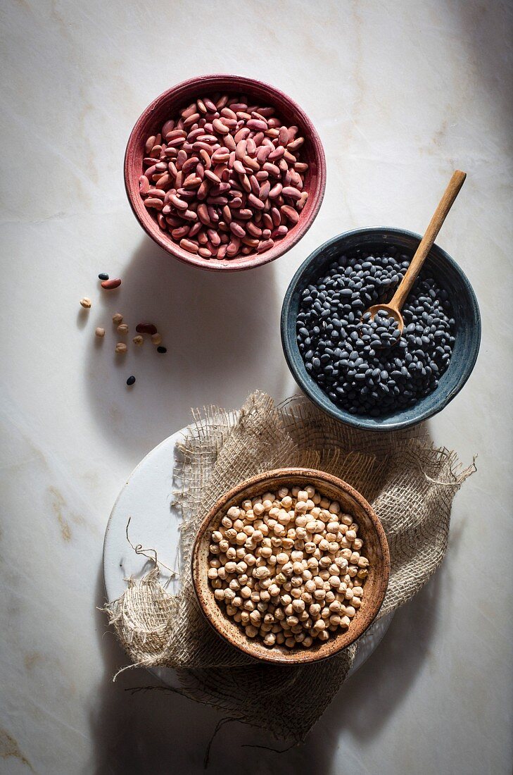 Chickpeas, kidney beans, black beans in individual ceramic bowls on a marble table