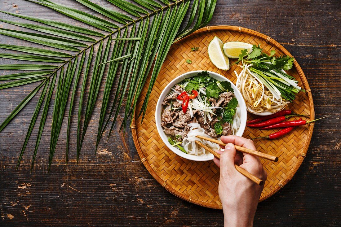 Person isst Pho Bo (Suppe mit Rindfleisch und Reisnudeln, Vietnam)