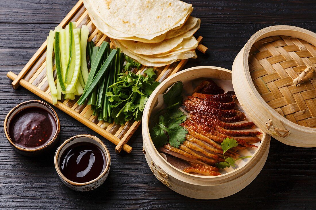Peking Duck in bamboo steamer served with fresh cucumber, green onions, cilantro and roasted wheaten chinese pancakes