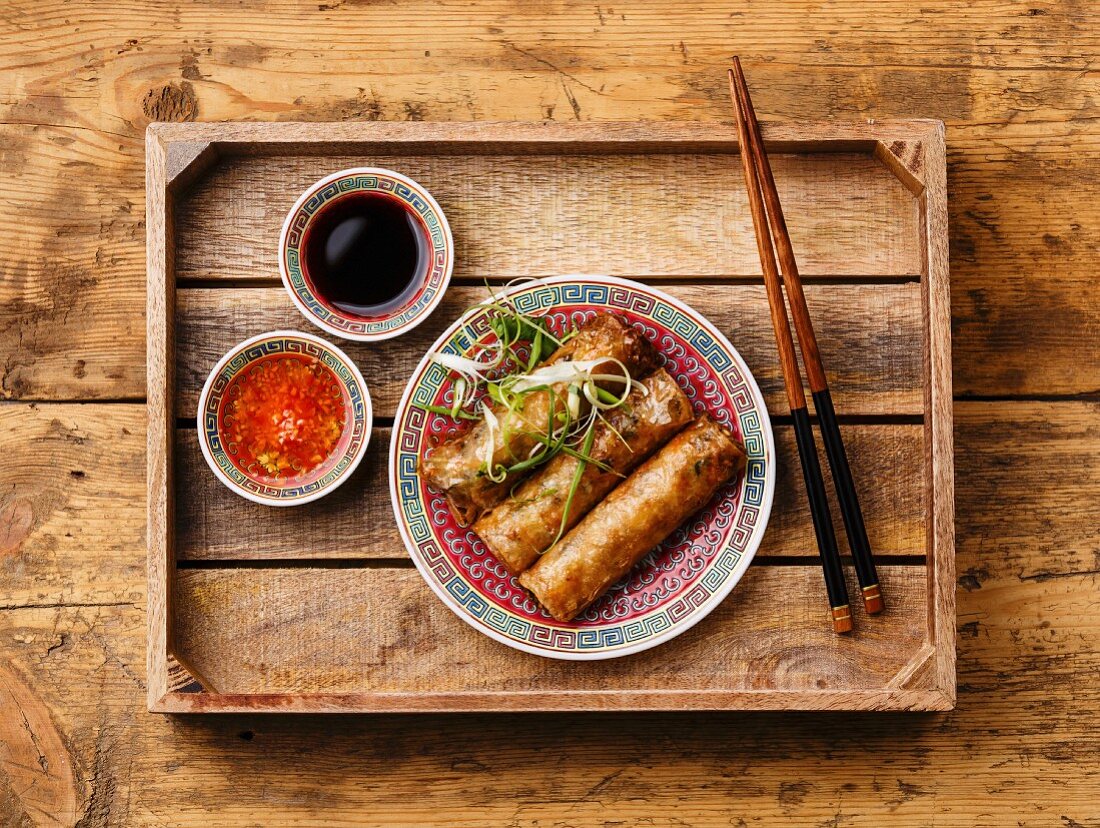 Spring rolls with sauce in wooden tray on wooden background