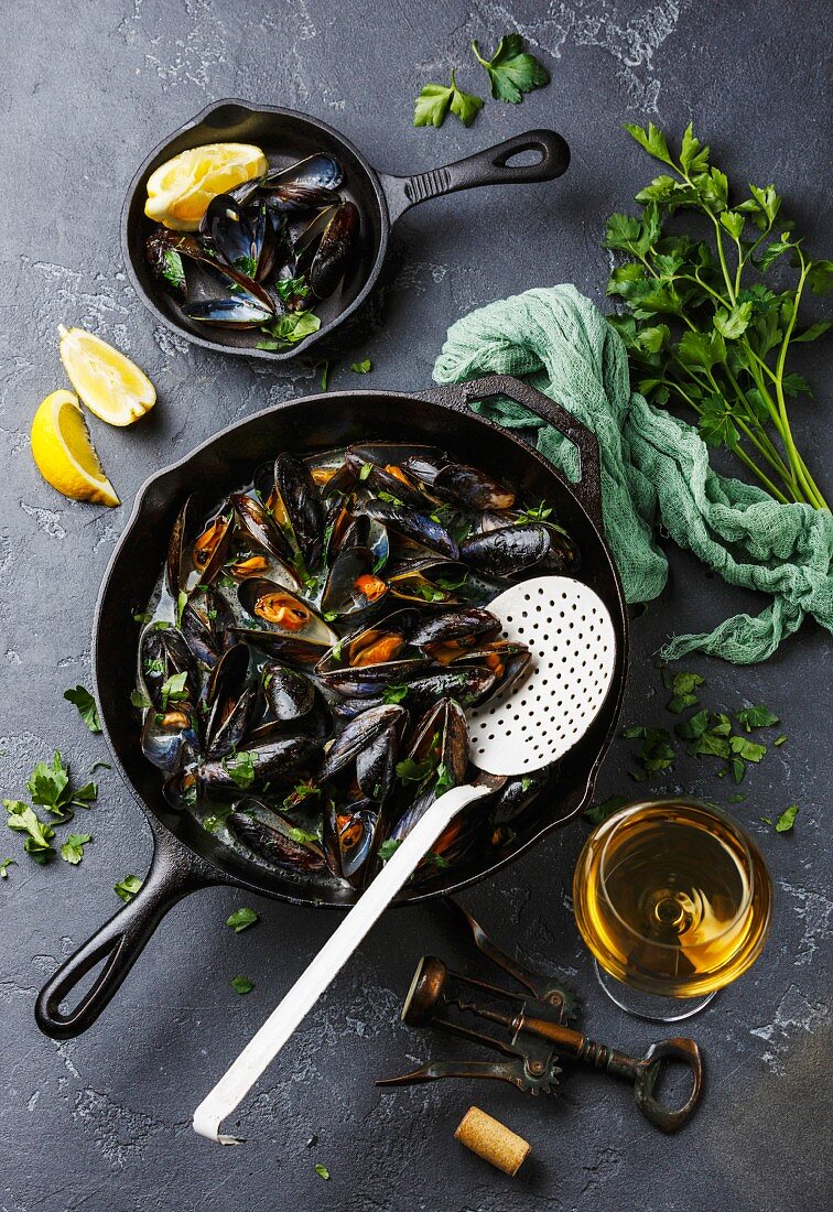 Mussels in black cooking pan with parsley and wine on dark stone background