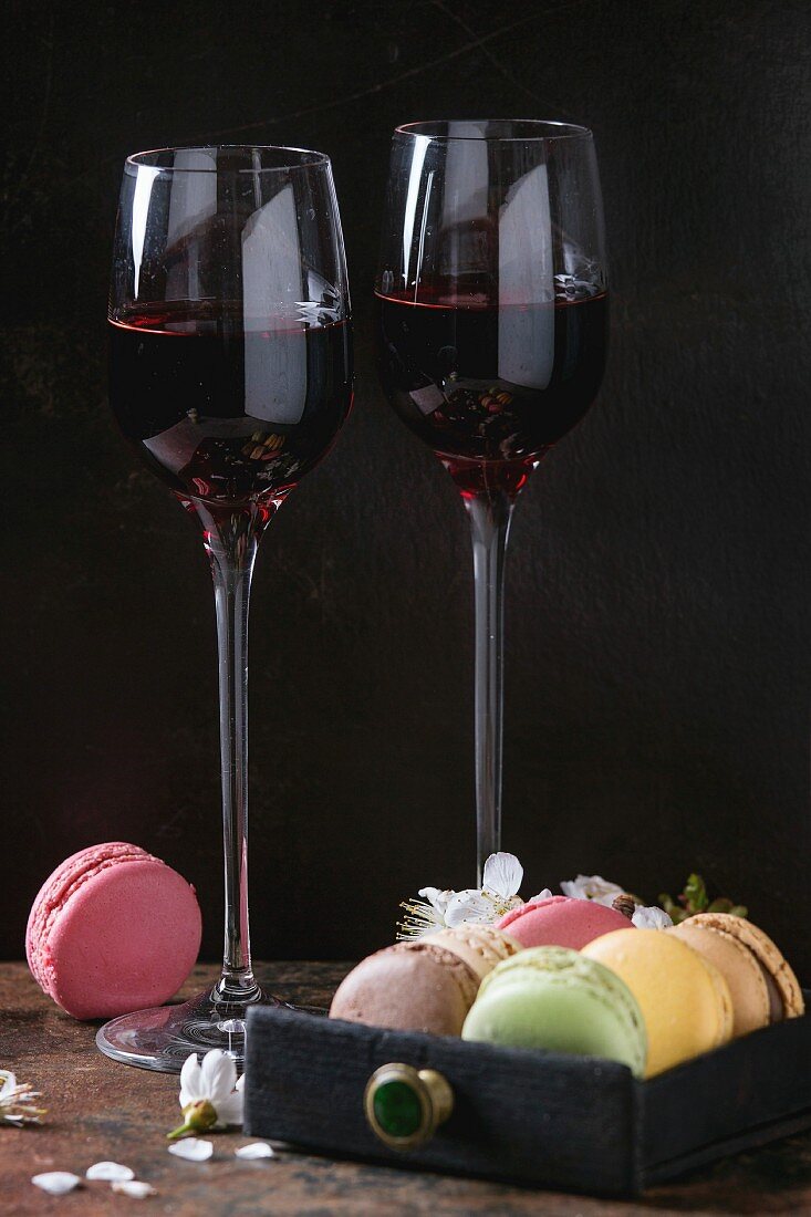 Two glasses of port wine with variety of colorful french sweet dessert macaroons with different fillings