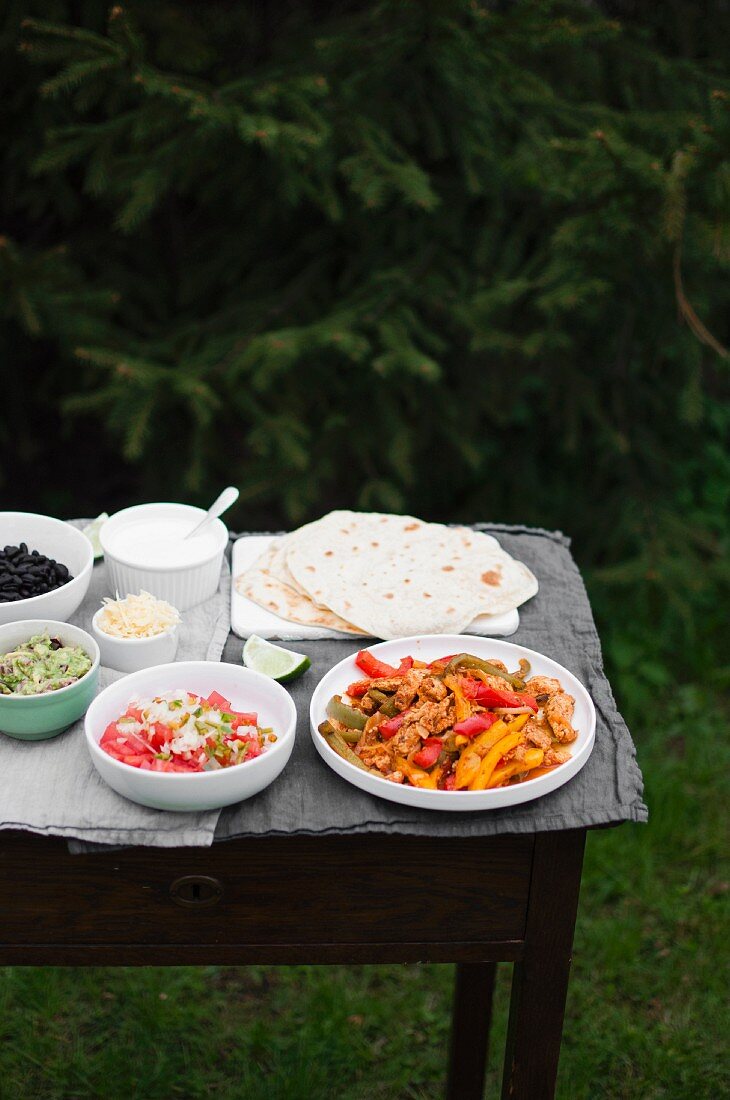 Chicken fajitas served with tortillas, pico de gallo, guacamole, black beans, grated cheese, sour cream and piece of lime