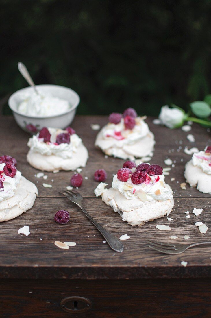 Mini pavlova (meringue) served with whipped cream, raspberries and almond flakes