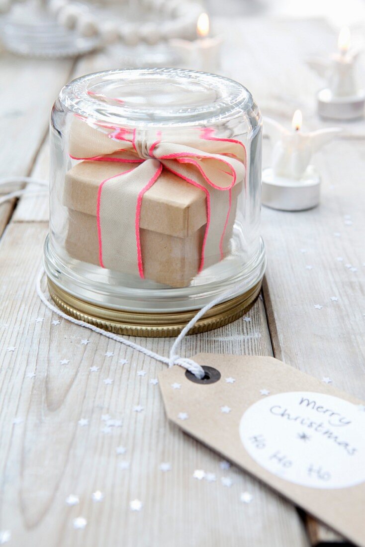 Gift box with ribbon in screw-top jar with 'Merry Christmas' tag