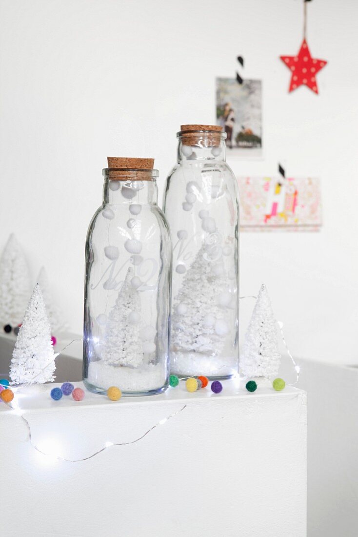 Small white tree decorations in glass bottles, artificial snow, colourful felt balls and fairy lights