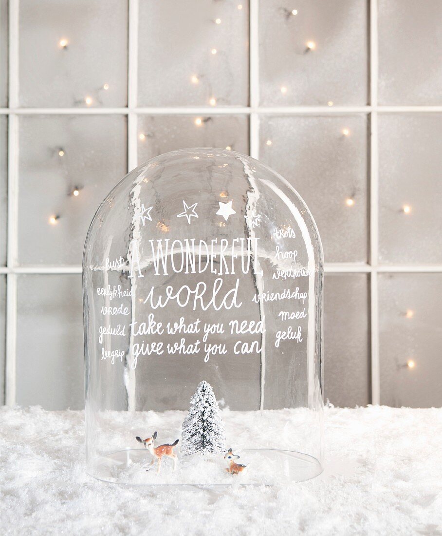 Two deer figurines and small tree under glass cover decorated with lettering in festive ambiance