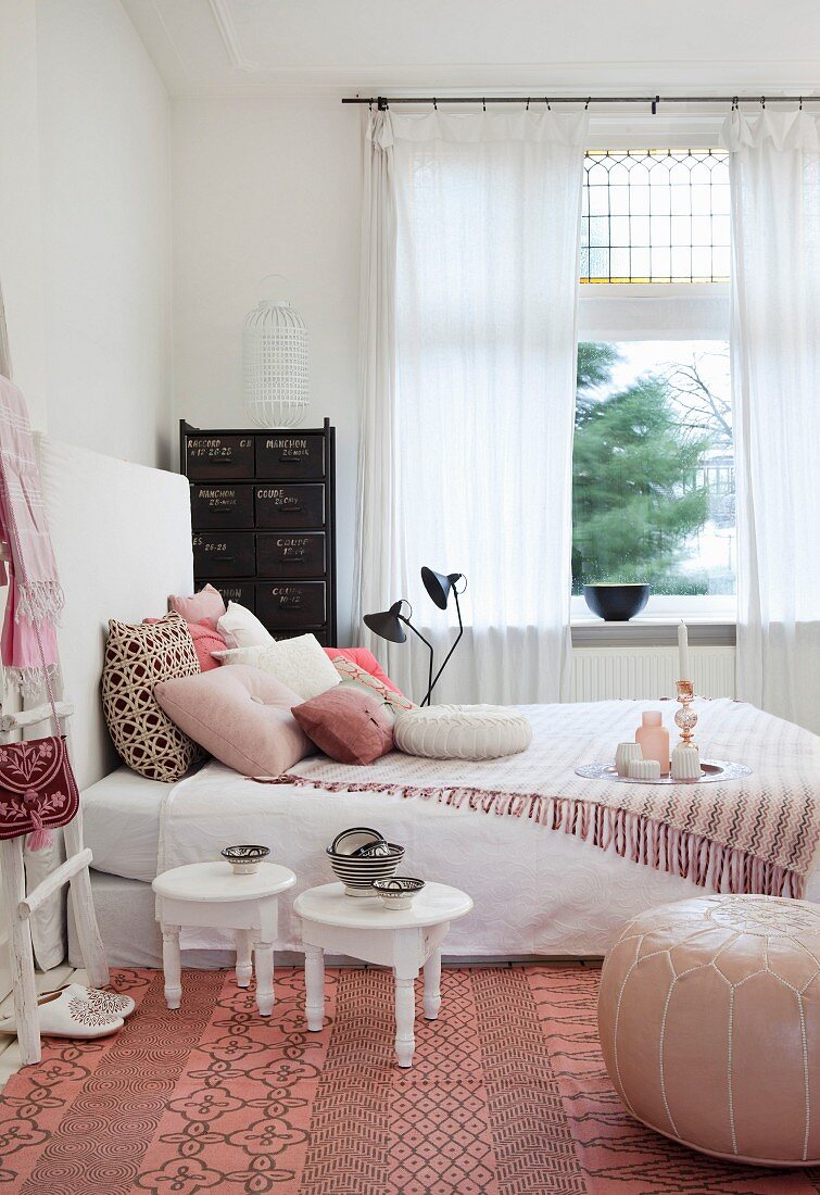 Feminines Schlafzimmer mit weißen Holztischchen, Leder-Pouf und Fransendecke auf Bett