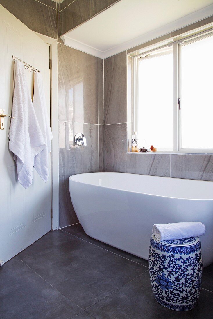 White bathtub and blue and white ceramic drum stool in modernised bathroom