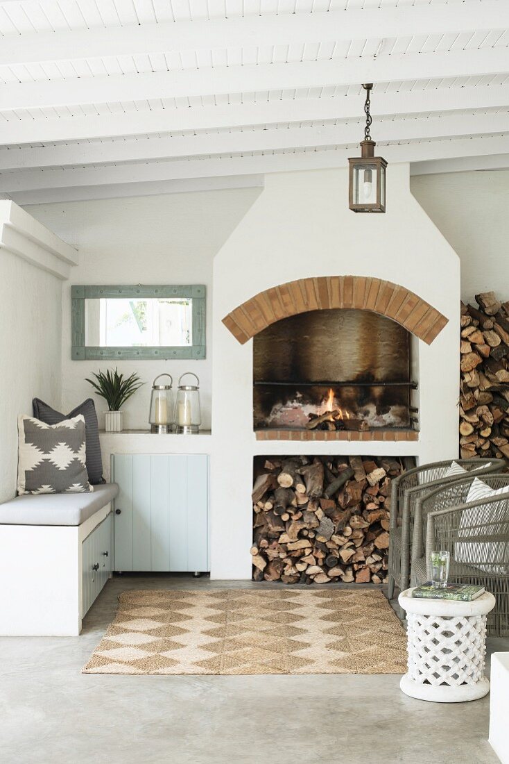 Firewood stacked below fireplace and lounge furniture on roofed veranda