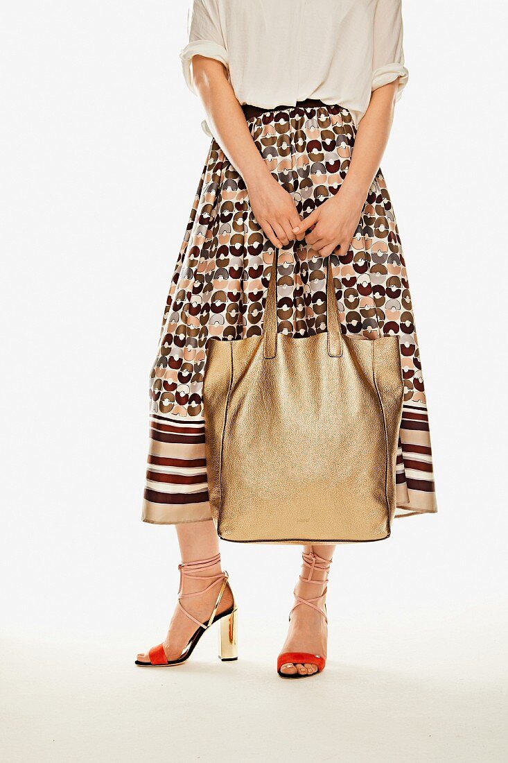 Frau in Midi-Rock mit Muster, goldfarbenem Leder-Shopper und Sandaletten mit Schnürung