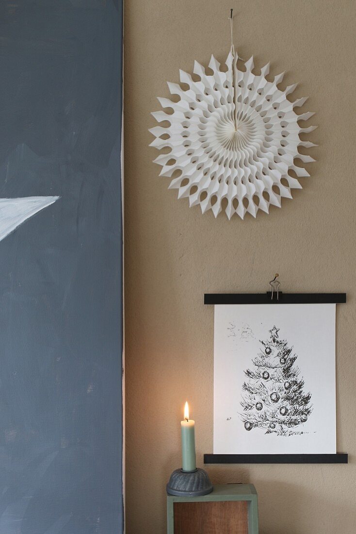 Weihnachtlich gestaltete Wand mit Bild, Papierstern und brennender Kerze
