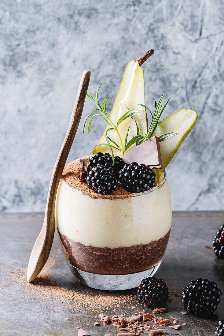 Dessert breakfast layered chia seeds, chocolate pudding, rice porridge in glass decorated by fresh blackberries, sliced pear, cocoa powder