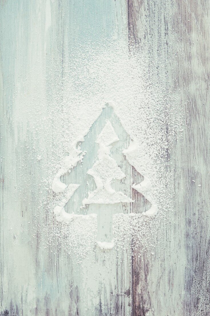 A fir tree drawn in powdered sugar on a white wooden background