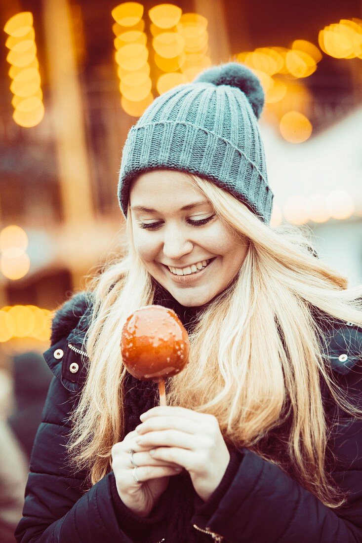 Winterlich gekleidete junge Frau mit Liebesapfel auf Weihnachtsmarkt