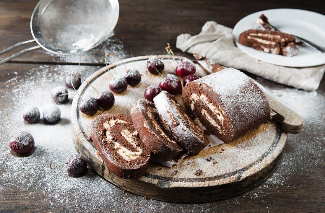 Chocolate swiss roll whole and chopped into slices with cherries and icing sugar