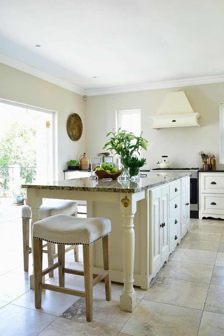 Elegant island counter and white bar stools on large stone flags in kitchen