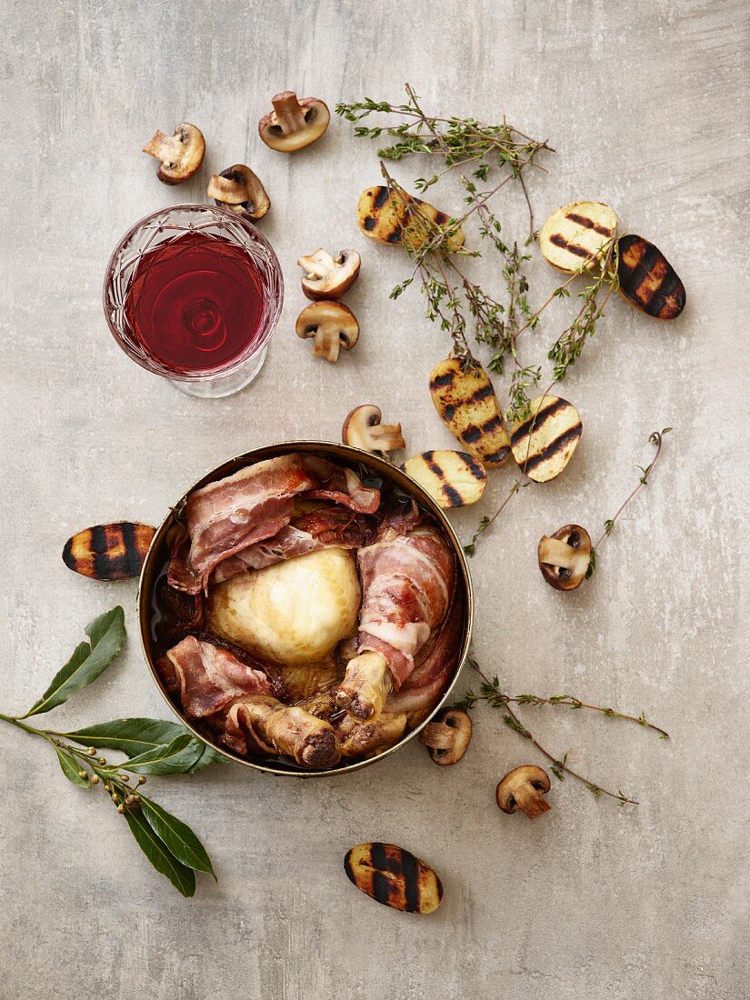 Coq au Vin mit gegrillten Kartoffelhälften, Champignons, Thymian und Rotweinglas