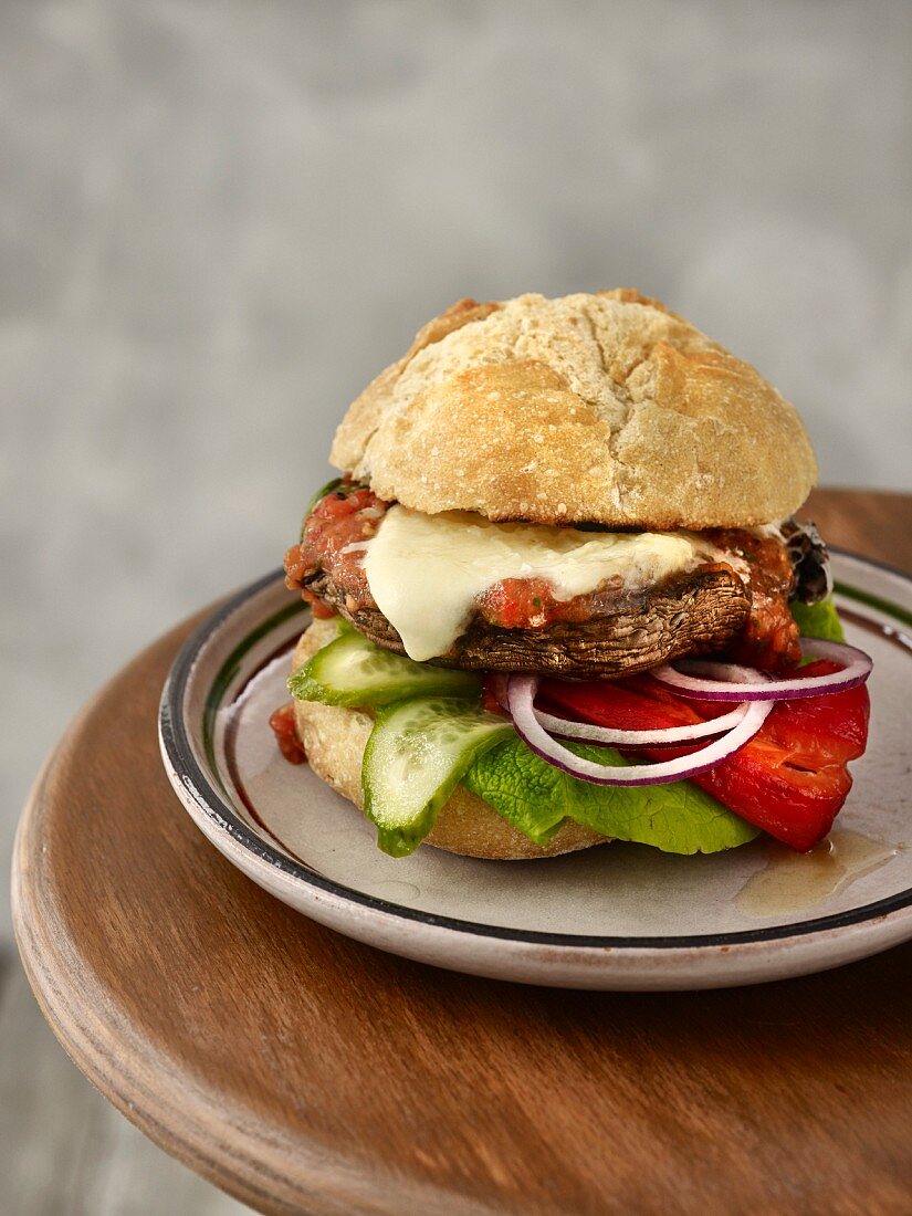 A portobello burger with grilled peppers, cucumber slices, red onion rings, mozzarella, and tomato and pepper salsa