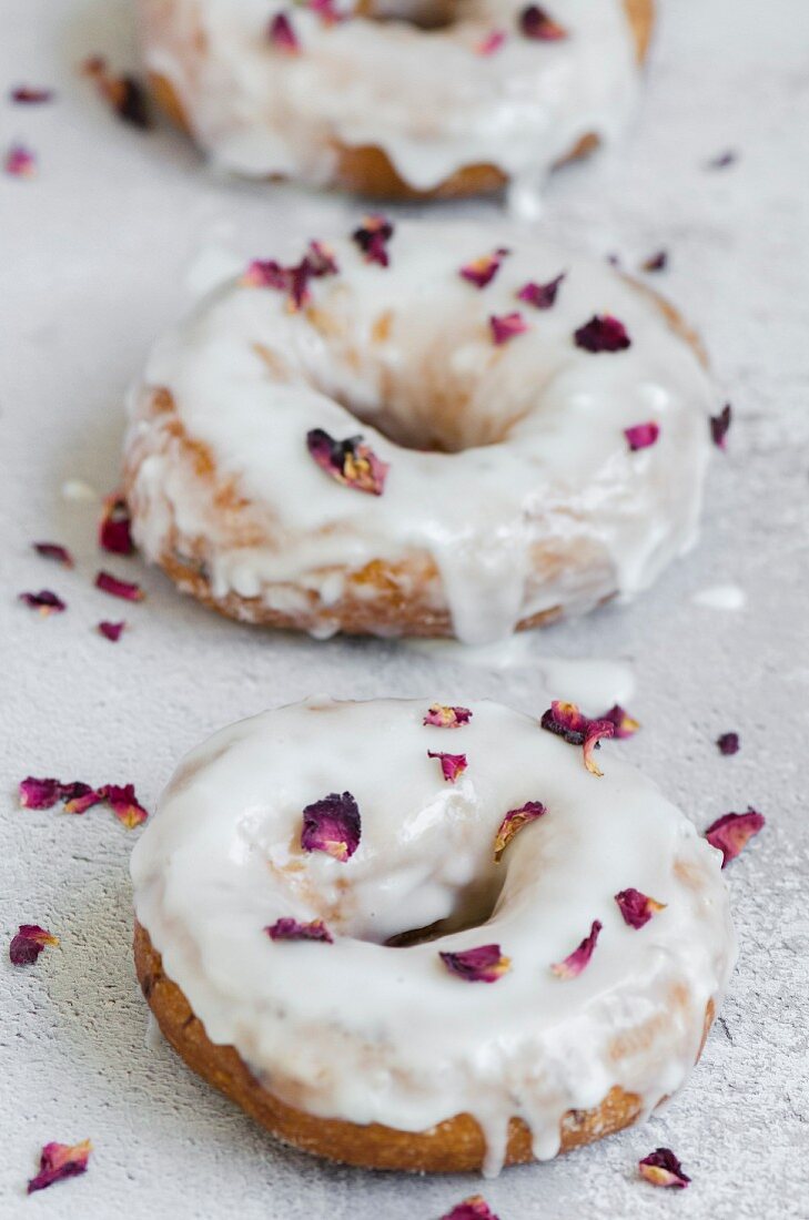 Drei Doughnuts mit Zuckerglasur und getrockneten Rosenblättern