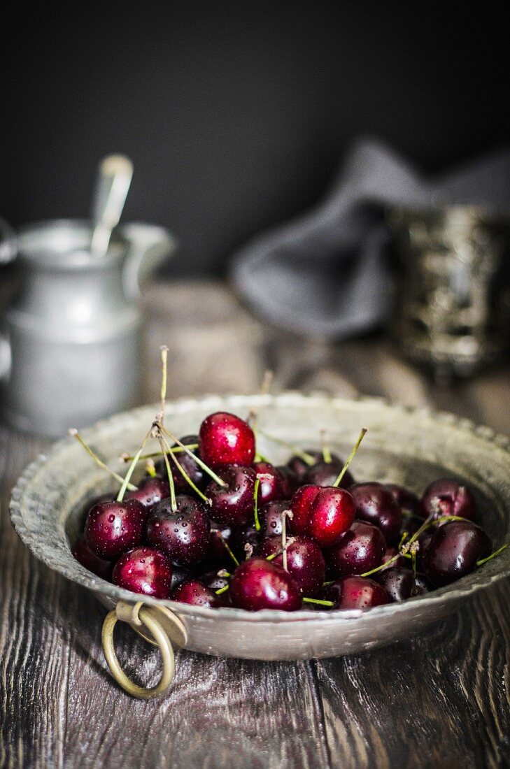 Freshly washed red summer cherries in a pewter bowl with jug