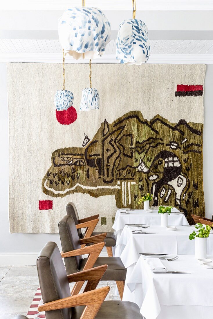 Gedeckte Tische im Restaurant mit abstraktem Wandteppich