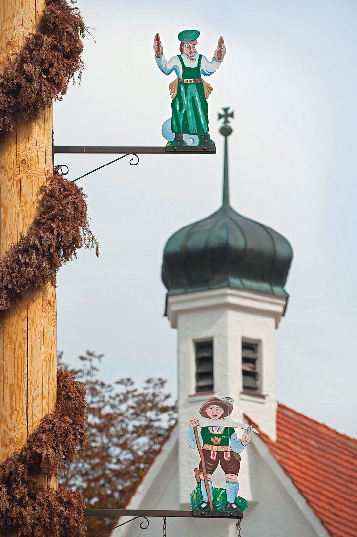 Maibaum-Pfahl mit Handwerker-Figuren auf dem Kirchplatz von Weiler, Bayern, Allgäu