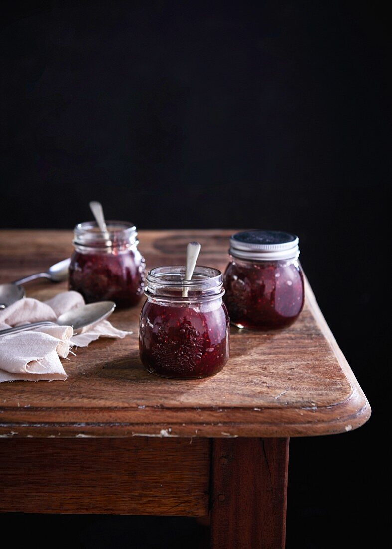 Raspberry jam in three screw top glass jars on a wooden table