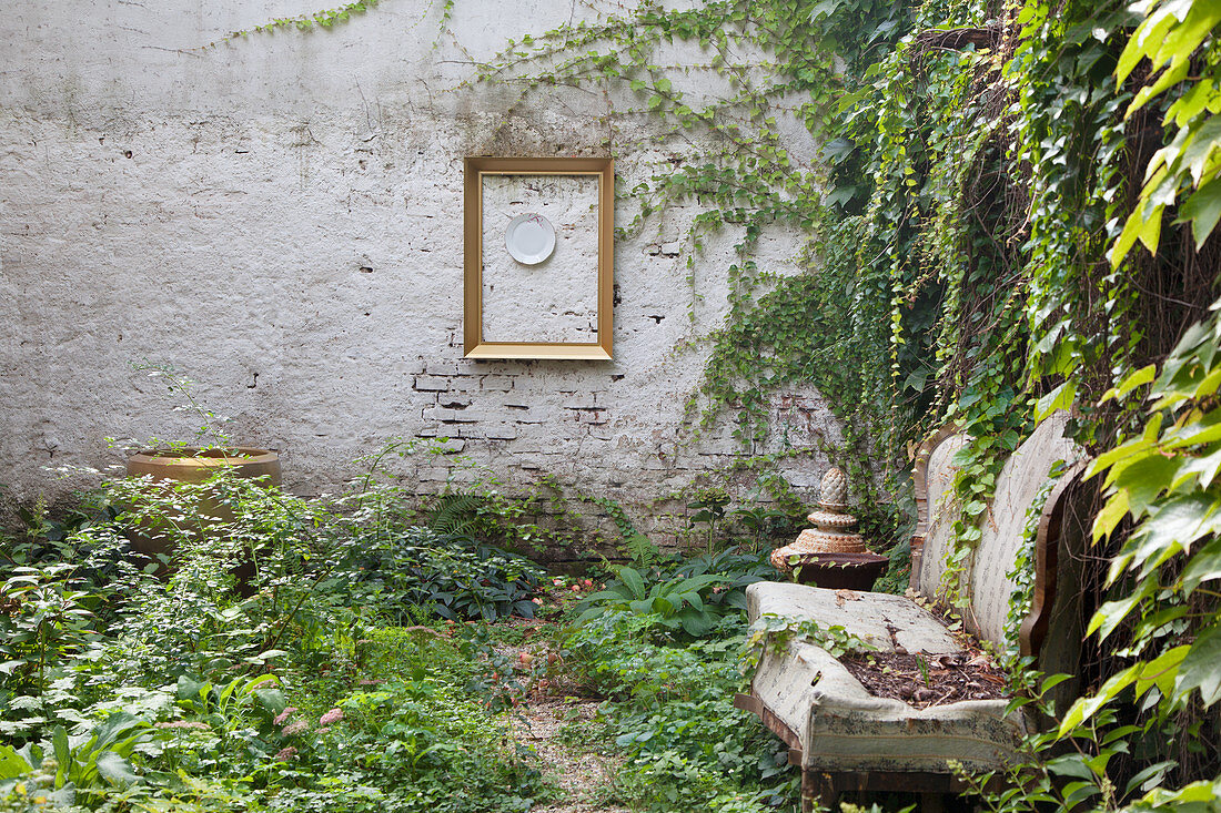 Old sofa in courtyard with Virginia creeper growing over garden wall