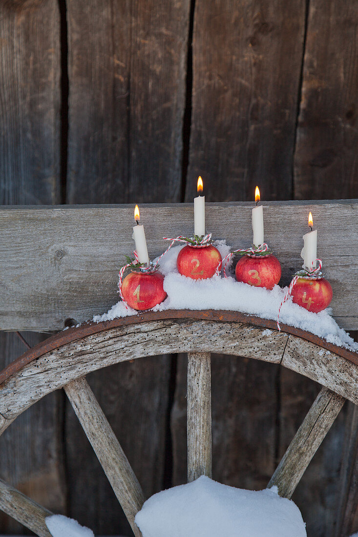 Kerzen stecken in nummerierten Äpfeln als Adventskranz