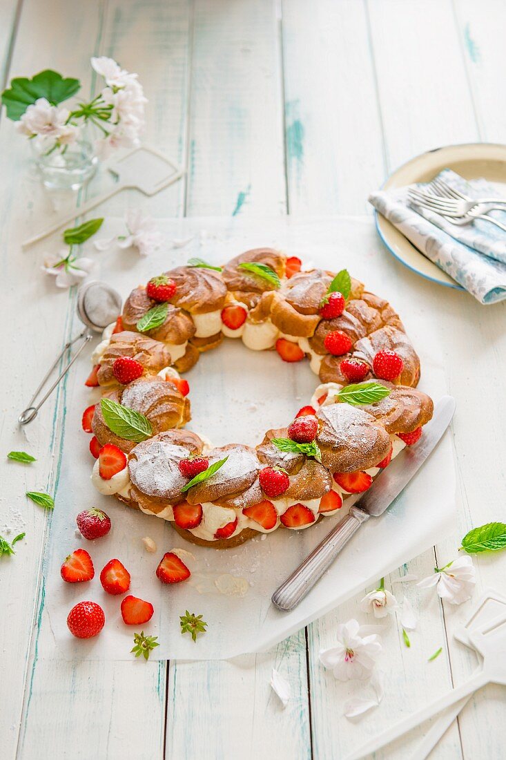 Profiterole wreath with whipped cream and strawberries with fresh mint